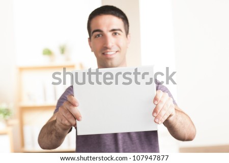 Attractive young man holding a blank white sign out in front of his body. Sign is in focus and face is out of focus.