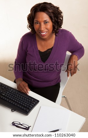 Beautiful African American female executive with dark brown hair at work in an office setting wearing a purple sweater.