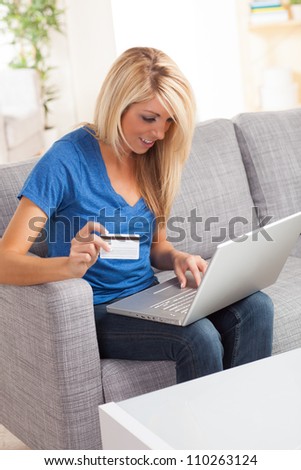 Sexy American woman sitting on couch with laptop doing online shopping wearing a blue shirt.