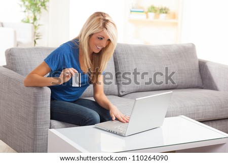 Sexy American woman sitting on couch with laptop doing online shopping wearing a blue shirt.