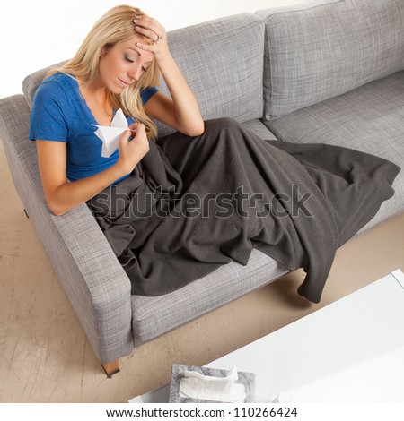 Pretty blond white female sitting on couch with a cold with gray blanket.