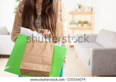 Cute young Latina woman holding shopping bags wearing yellow shirt with flowers and jean shorts.
