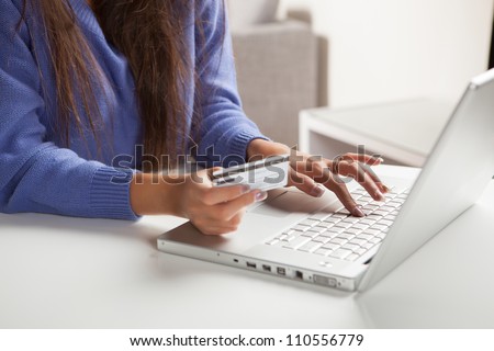 Sweet young Hispanic female using computer for online shopping holding credit card.