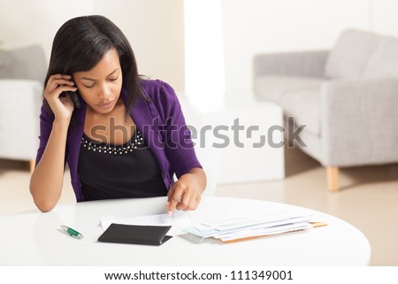 Attractive young African American woman working on finances at home wearing purple jacket sitting at dining table.