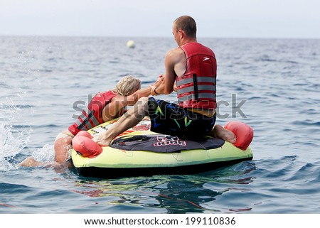 HALKIDIKI, GREECE- MAY 26, 2014: Unrecognized man helping woman to get on water inflatable. 20 million tourists expected to visit the beaches, making it a record, in Halkidiki, Greece.