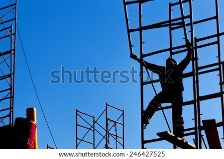 silhouette of construction worker against sky on scaffolding with ladder on building site