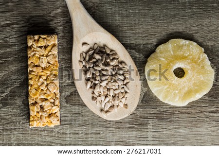 Seeds in Wooden Spoon Spread on Wood Background with energy bar and dried pineapple.