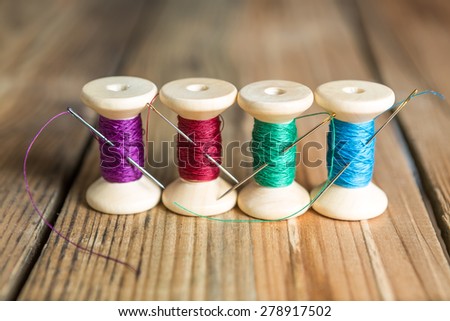 Spools of thread with needles on wooden background. Old sewing accessories. colored threads