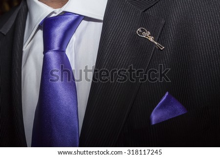 Man in black suit with purple tie and broach