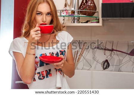 Cute female with freckles drinking coffee from cup in kitchen