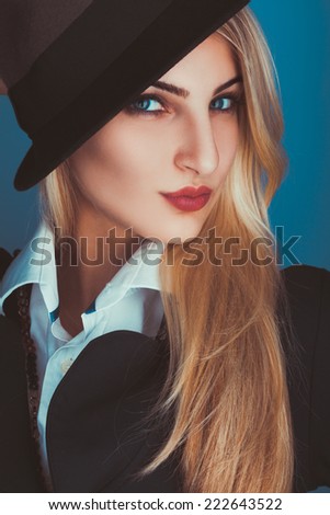 Charming blonde woman in black hat looking at camera in studio