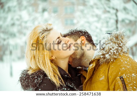 passionate guy kisses girl with white hair in neck on street in snow. Horizontal color photo