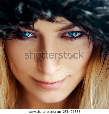 Square portrait of cutie young woman with blond hair and blue eyes in fur hat. Color high contrast photo