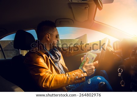 Fashion model male driving car with lot of money in hand. Inside photo
