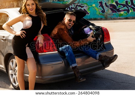 awesome couple enjoys bag full of money in trunk of car outdoors