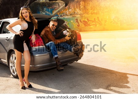 cheerful beautiful couple enjoys a bag full of money sitting in the trunk of a car outdoors