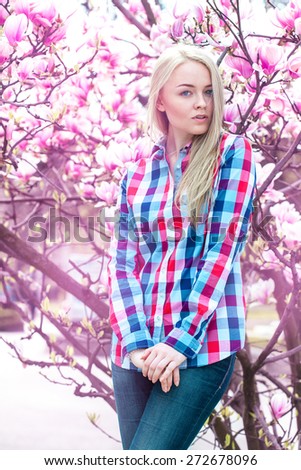 Vertical portrait of modest young blonde girl with pink flowers. Spring time