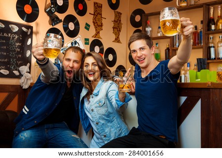 fun company of two boys and one girl drink in bar. horizontal photo