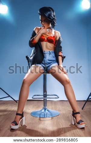 young sexual woman suck finger and posing on chair in studio on blue background