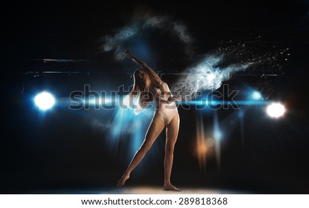 Lovely slim blonde ballet dancer on stage in theater posing against spotlights