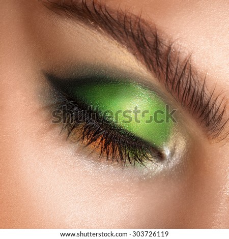 macro photo of closed eyes with professional green colors makeup. square. studio shot.