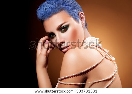 Short blue hairstyle and green makeup of female in studio. orange background. horizontal