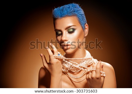 Sensual portrait of young woman with pearls short blue hairstyle and green makeup. Studio shot. orange background