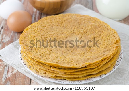 Stack of crepes made ??of corn flour on a plate and baking ingredients (eggs, flour, milk)