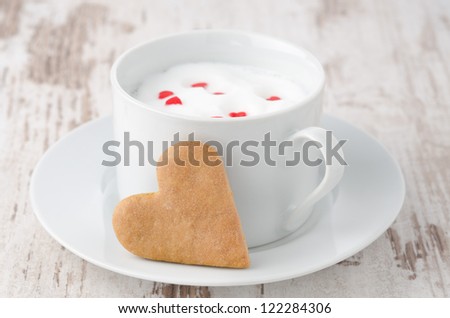 cup of hot milk with foam, decorated with sugar hearts and heart-shaped cookies on the table