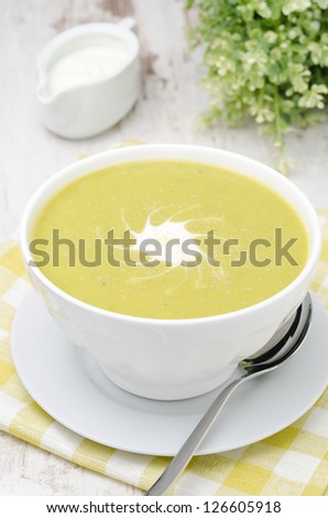 bowl of green pea soup with ginger and cream in a white bowl, closeup, vertical
