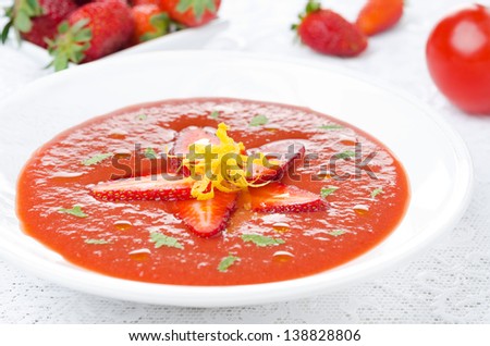 tomato and strawberry gazpacho in a plate, fresh berries and tomatoes in the background, horizontal close-up