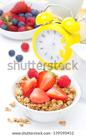 Breakfast - granola with fresh berries, milk and yellow alarm clock on white
