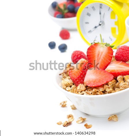 Granola with fresh berries for breakfast and yellow alarm clock on white background close-up