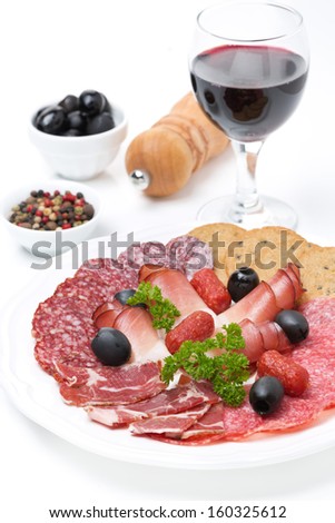 Assorted meat delicacies on a plate, pepper, olives and a glass of wine, vertical