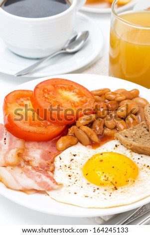 Traditional English breakfast with fried eggs, bacon, beans, coffee and juice, close-up