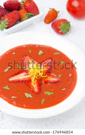 tomato and strawberry gazpacho in a plate, fresh berries and tomatoes in the background, vertical top view