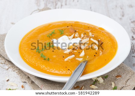 carrot soup with almonds, yogurt and watercress on white wooden table, close-up