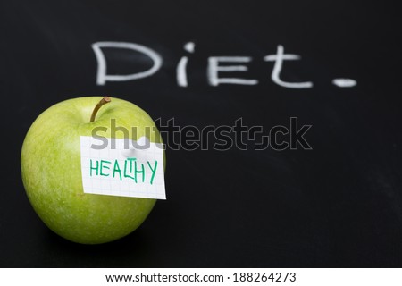 green apple with label on a black background and the word diet, written in chalk, concept