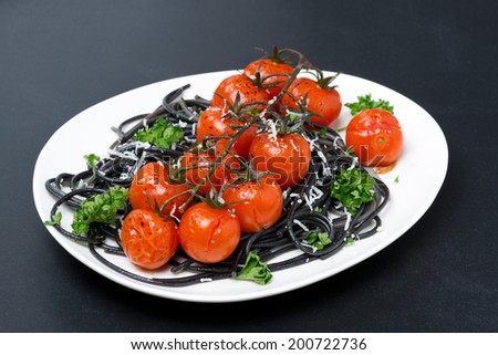 plate of black pasta with baked tomatoes, parmesan cheese on a black background, close-up