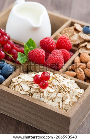 box with breakfast items - oatmeal, granola, nuts, berries and milk, vertical, close-up, top view