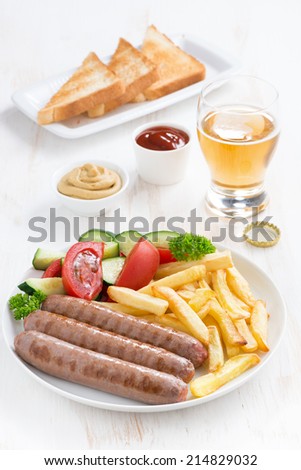 grilled sausages with French fries, vegetables and glass of beer, vertical, top view