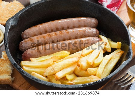 grilled sausages with French fries in a frying pan, close-up