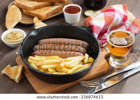 grilled sausages with French fries  in a frying pan, toasts and beer, top view