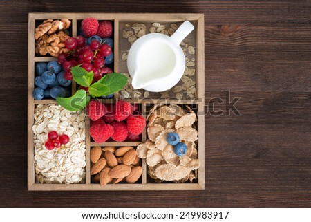 wooden box with breakfast items - oatmeal, granola, nuts, berries and milk, top view, horizontal, close-up