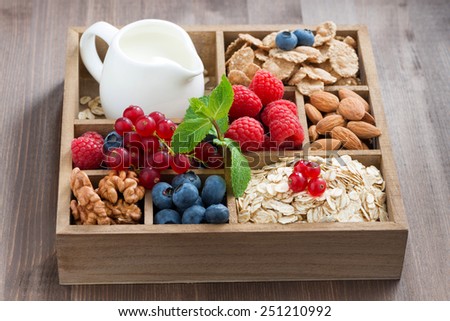 wooden box with breakfast items - oatmeal, granola, nuts, berries and milk on table