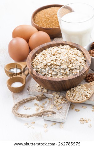 oat flakes and ingredients on a white wooden table, vertical, close-up