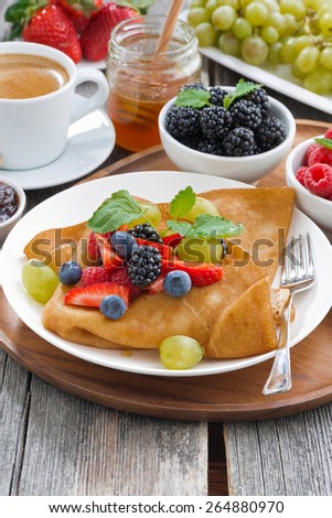 breakfast - crepes with fresh berries and honey, coffee on wooden background, vertical, top view