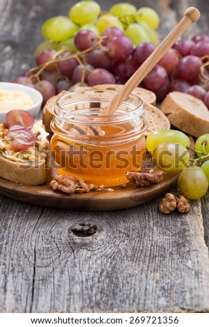 flavored honey, bread and butter and grapes on a wooden background, vertical