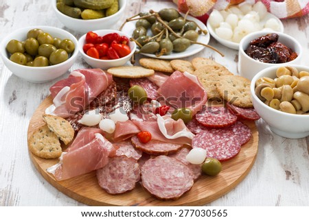 Assorted meat snacks, sausages and pickles on wooden board, horizontal