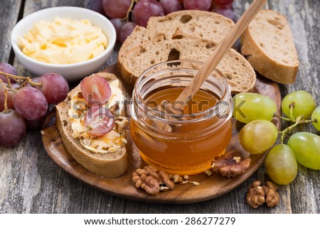 flavored honey, bread with butter and grape on wooden board, top view